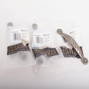 May include: A selection of cabinet hardware, including two small knobs and a decorative handle. The knobs are round with a matte finish, and the handle features an embossed leaf design. Each piece is packaged in a clear plastic bag.