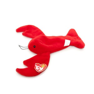 May include: A plush red lobster toy with black thread whiskers and a TY heart-shaped tag. The lobster has two large claws and a segmented body. The toy is made of soft material and is designed to resemble a lobster.