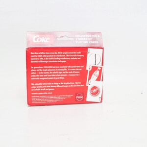 May include: A red Coca-Cola collector's tin with two decks of playing cards. The tin features the Coca-Cola logo and text. The playing cards have Coca-Cola imagery.