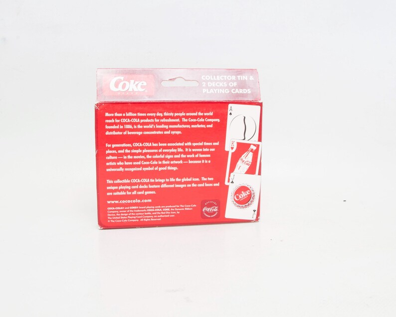 May include: A red Coca-Cola collector's tin with two decks of playing cards. The tin features the Coca-Cola logo and text. The playing cards have Coca-Cola imagery.