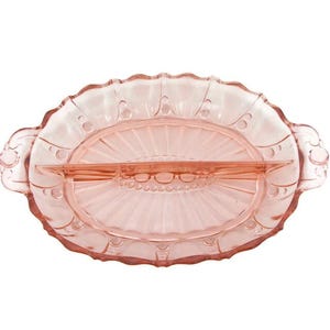 May include: A pink glass serving dish with an oval shape and a scalloped edge. The dish has a raised centre section and two handles. The design includes small, raised dots around the rim and a ribbed pattern in the centre.