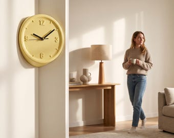 May include: A round, pale yellow wall clock with a smooth, matte finish, featuring raised numbers at the twelve, three, six, and nine o'clock positions, and two black hands mounted in the center, displayed on a white corner wall section.