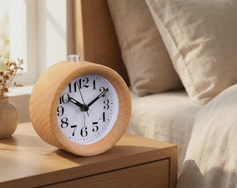 May include: A light-colored wooden alarm clock with a white face and black numerals sits on a wooden nightstand. The clock has a round shape and a silver top. The time is approximately 2:10. A small vase with dried flowers is to the left.