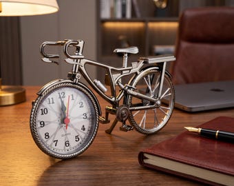 May include: A metallic bicycle-shaped table clock with a silver-toned frame and a round white clock face integrated into the front wheel. The clock features black Arabic numerals, a red second hand, and black hour and minute hands with the word QUARTZ.
