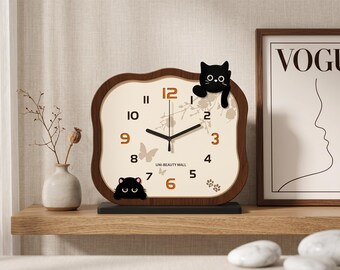 May include: A decorative wooden clock with a cream-colored face, featuring black cat accents. The clock has brown numerals and hands, with a black base. The text "UNI-BEAUTY MALL" is visible on the clock face.