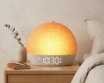 May include: A dome-shaped alarm clock with a warm, glowing orange fabric upper section and a light gray fabric base. The digital display shows the time 10:30 AM in white light, along with small icons for a snooze function, a musical note, and an alarm.