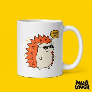 May include: White ceramic mug featuring a cartoon hedgehog wearing sunglasses. The hedgehog has orange spikes and is saying "LOOKING SHARP" in a speech bubble. The mug has a white handle and the words "MUG LAUGH" are at the bottom.