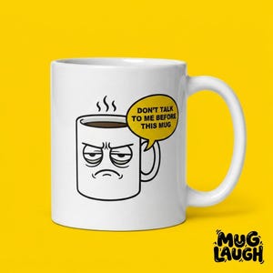 May include: White ceramic coffee mug with a grumpy face illustration and the text "DON'T TALK TO ME BEFORE THIS MUG" in a yellow speech bubble. The mug has a handle and is filled with coffee. The background is yellow.
