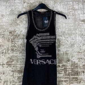 May include: Black tank top with a rhinestone-studded design. The top features the Versace logo in rhinestones and a rhinestone-lined neckline. The tank top is hanging on a black hanger.
