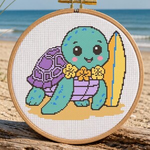 May include: A cross-stitch embroidery of a cartoon turtle with a surfboard, set in a wooden hoop. The turtle is teal, purple, and yellow, with a flower lei. The background shows a beach with sand, ocean, and blue sky.