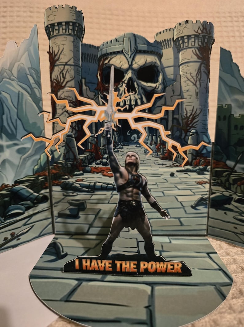 Puede incluir: Tarjeta desplegable con una figura musculosa sosteniendo una espada, con un fondo de castillo y el texto "I HAVE THE POWER". La tarjeta tiene una combinaci&oacute;n de colores gris y naranja.
