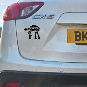 Op de afbeelding: Een zwarte vinyl sticker aangebracht op de achterkant van een witte Mazda CX-5. De sticker toont een silhouet van een AT-AT walker uit Star Wars met de tekst "MY OTHER RIDE IS AN AT-AT" in witte letters op het lichaam van de walker.