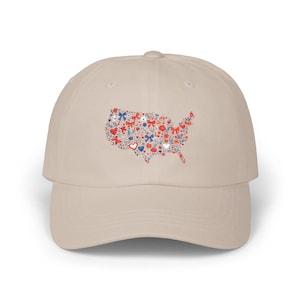May include: A beige baseball cap with a design of the United States made up of red, white, and blue floral and heart patterns. The cap has a curved peak and an adjustable strap at the back. The design evokes a patriotic theme.
