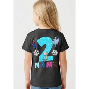 Op de afbeelding: Zwart T-shirt met een groot blauw cijfer 2, versierd met sneeuwvlokken en stripfiguren. Het woord "NAME" staat onder het cijfer in kleurrijke letters. Een ontwerp met een verjaardagsthema.