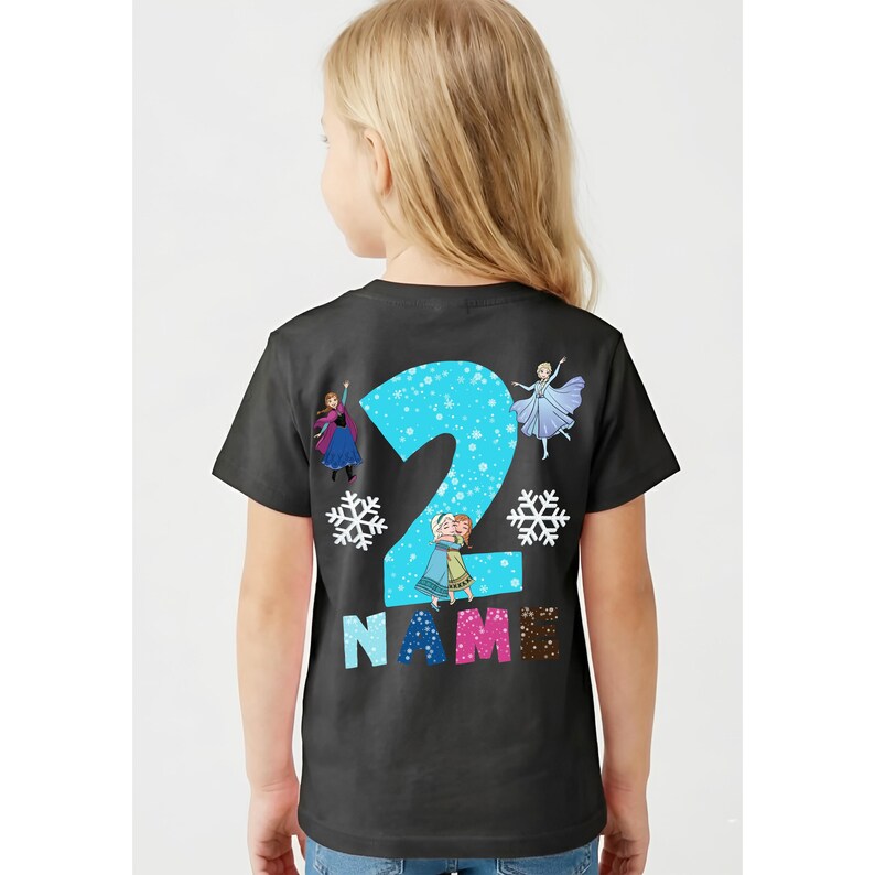 Op de afbeelding: Zwart T-shirt met een groot blauw cijfer 2, versierd met sneeuwvlokken en stripfiguren. Het woord "NAME" staat onder het cijfer in kleurrijke letters. Een ontwerp met een verjaardagsthema.