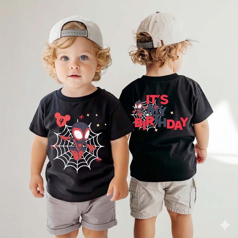 Op de afbeelding: Zwart T-shirt met een Spider-Man-afbeelding op de voorkant en de tekst "IT'S MY BIRTHDAY" op de achterkant. Het ontwerp bevat een spinnenweb en sterren. Het shirt wordt gecombineerd met grijze shorts en een lichtgekleurde baseballcap.