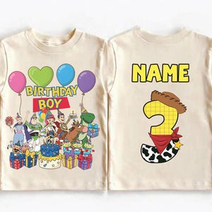 Op de afbeelding: Een cr&egrave;mekleurig T-shirt met een kleurrijke afbeelding van Toy Story-personages, ballonnen en de woorden "BIRTHDAY BOY". De achterkant van het shirt heeft het woord "NAME" boven een nummer 3 met een cowboyhoed en bandana.