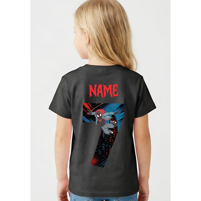K&ouml;nnte beinhalten: Schwarzes T-Shirt mit einer Grafik eines Superhelden, der Zahl 7 und dem Wort "NAME" in Rot. Der Superheld wird in Aktion vor einer Stadtkulisse mit roten und blauen Details dargestellt. Dieses T-Shirt ist f&uuml;r Kinder konzipiert.