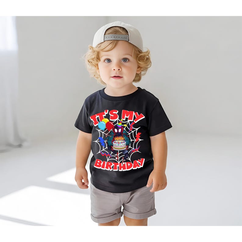 K&ouml;nnte beinhalten: Ein schwarzes T-Shirt mit dem Text "IT'S MY BIRTHDAY" in Rot und Wei&szlig;, das eine Cartoon-Spinne mit einer Geburtstagstorte zeigt. Das T-Shirt wird von einem kleinen Kind getragen, kombiniert mit grauen Shorts und einer beigen Baseballkappe.