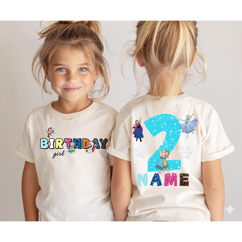 Op de afbeelding: Een cr&egrave;mekleurig T-shirt met de tekst "BIRTHDAY girl" in kleurrijke letters en cartoonfiguren. De achterkant van het shirt toont een groot blauw nummer "2" met karakterillustraties en het woord "NAME".