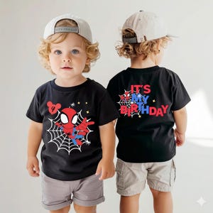 Op de afbeelding: Zwart T-shirt met een Spider-Man-afbeelding en webdesign, met het nummer "4". De achterkant van het shirt zegt "IT'S MY BIRTHDAY" in rood en blauw. De outfit bevat grijze shorts en een lichtgekleurde baseballcap.