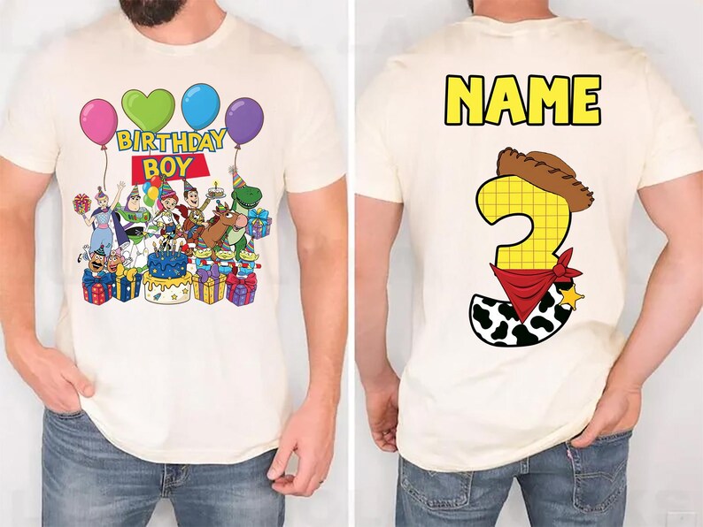 Op de afbeelding: Cr&egrave;mekleurig T-shirt met een kleurrijke afbeelding van Toy Story-personages, ballonnen en de tekst "BIRTHDAY BOY" op de voorkant. De achterkant van het shirt toont het woord "NAME" en het cijfer 3 met een cowboyhoed en bandana.