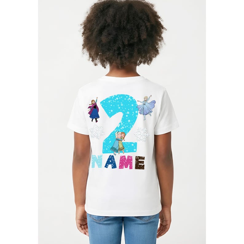 Op de afbeelding: Wit T-shirt met een groot blauw nummer 2, sneeuwvlokkenpatroon en tekenfilmfiguren. Het woord "NAME" staat eronder in kleurrijke letters. Het shirt is ontworpen voor een kind.