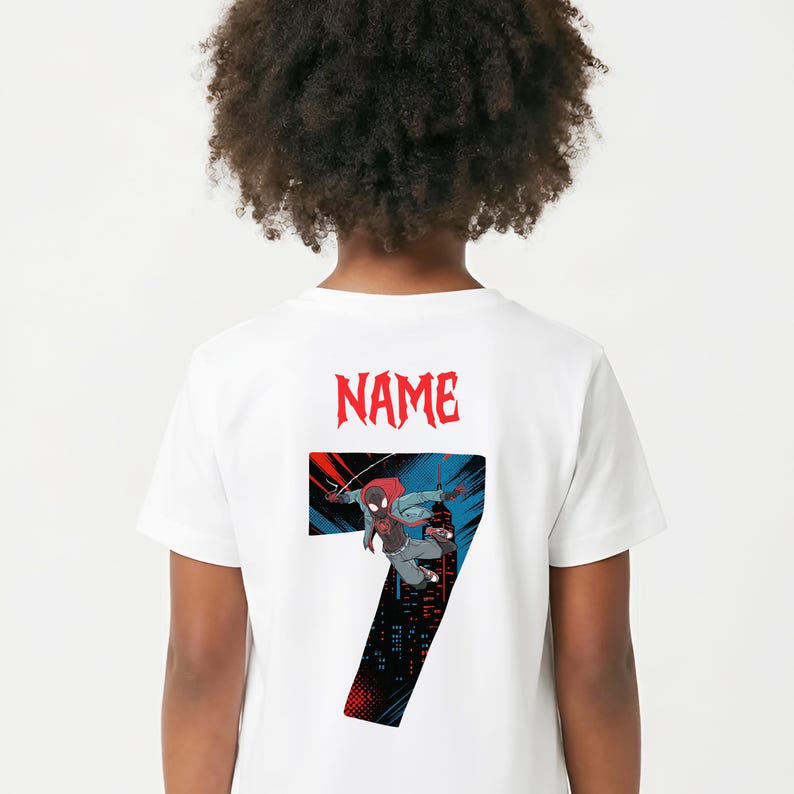 K&ouml;nnte beinhalten: Wei&szlig;es T-Shirt mit einer Grafik eines Superhelden und der Zahl 7. Der Superheld ist in einer dynamischen Pose dargestellt, mit roter und schwarzer Farbgebung. Das Wort "NAME" ist rot &uuml;ber der Zahl gedruckt.