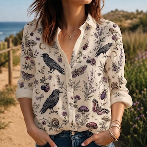 May include: A long-sleeve button-down shirt in an off-white color featuring a detailed print of black ravens, various mushrooms, purple butterflies, beetles, snails, blackberries, and sprigs of lavender scattered across the fabric.
