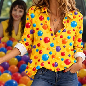May include: A long-sleeved button-down shirt in bright yellow featuring a vibrant, multi-colored polka dot pattern in shades of red, blue, orange, and purple. The shirt has a classic collar, white buttons, and cuffs rolled up to the elbows.