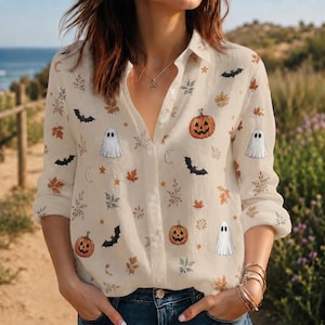 Op de afbeelding: Een beige overhemd met lange mouwen en knoopsluiting, voorzien van een all-over print met oranje pompoenen, witte spoken, zwarte vleermuizen, bruine herfstbladeren, kleine sterretjes en maansikkels, afgewerkt met een klassieke kraag.