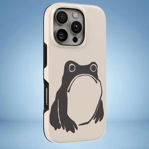 Peut inclure: Une coque de smartphone couleur crème avec une illustration graphique gris foncé d'une grenouille au dos. La coque présente un contour noir sur les bords et une découpe pour le système de triple objectif photo situé en haut à gauche.
