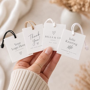 Op de afbeelding: Vier vierkante witte papieren labels met zwarte tekst en afbeeldingen, waaronder 'Your Logo Here', 'Thank You!', 'BELLA & CO EST. 2024' en 'Jolie Knitting HANDMADE WITH LOVE'. Elk label is voorzien van een lusje van touw of koord.
