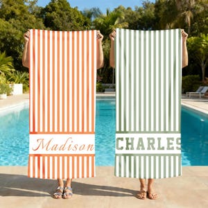May include: Two personalized beach towels with vertical stripes. One is orange and white, the other is green and white. The orange towel has the name "Madison" printed on it, and the green towel has the name "Charles" printed on it.