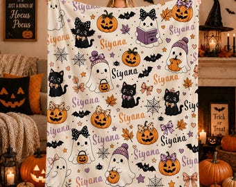 Könnte beinhalten: Eine cremefarbene Fleecedecke mit einem wiederkehrenden Halloween-Muster aus Geistern, schwarzen Katzen und Kürbissen. Das Design enthält den Namen Siyana in Lila und Orange sowie Spinnennetze, Fledermäuse, Schleifen und Herbstblätter.