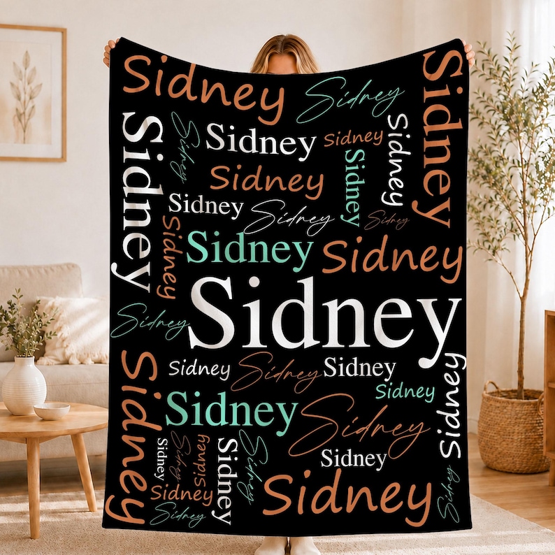 May include: A black rectangular throw blanket featuring the name Sidney printed repeatedly in various sizes, orientations, and fonts. The text appears in white, light blue, and peach colors, creating a layered, collage-style pattern.