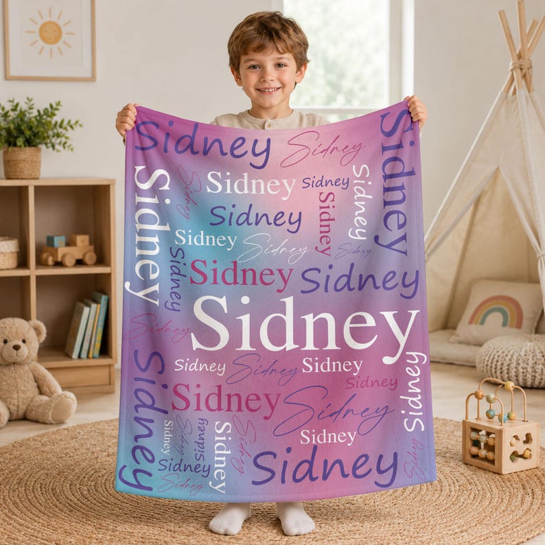 May include: A soft, rectangular fleece blanket featuring a vibrant gradient background that transitions from blue to purple and pink. The name Sidney is printed repeatedly across the surface in various white, purple, and pink fonts.