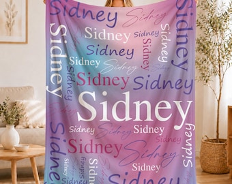 Könnte beinhalten: Eine weiche Fleecedecke mit einem Farbverlaufshintergrund, der von Hellblau zu Violett und Pink übergeht. Der Name Sidney ist mehrfach in verschiedenen Schriftarten, Größen und Ausrichtungen auf der Oberfläche in weißer, violetter und pinker Schrift gedruckt.