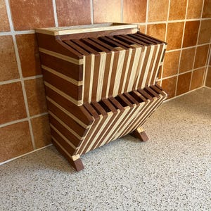May include: A wooden knife block with a striped design, featuring alternating light and dark wood. The block has multiple slots for knives and is designed to sit on a countertop. The color scheme is brown and beige.