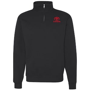 May include: Black quarter-zip sweatshirt with a red Toyota logo on the upper left chest. The sweatshirt has a high collar and a silver zipper. The Toyota logo is a stylized emblem with the brand name below it.