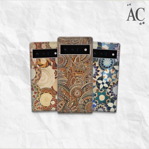 Può includere: Tre custodie per telefono con motivi unici e colorati. Le custodie presentano disegni intricati nelle tonalità del marrone, dell'arancione e del blu. Le custodie hanno una forma rettangolare con un ritaglio per la fotocamera nella parte superiore. Le lettere "AC" sono visibili in alto a destra.