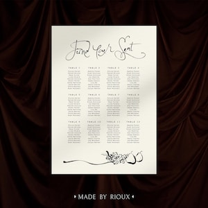 May include: A rectangular cream-colored seating chart sign featuring the black text Find Your Seat at the top, followed by twelve tables with lists of names. The bottom includes a black illustration of grapes and pears with the text MADE BY RIOUX.