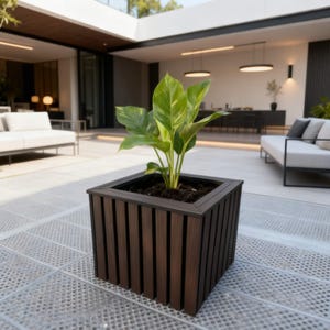 May include: A square, dark brown wooden planter box with vertical slats. The planter contains soil and a green plant with large leaves. The planter is outdoors on a patio.