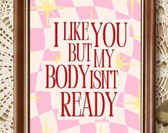 May include: A rectangular dark brown wooden frame containing a print with a pink and cream checkered background featuring yellow starburst shapes and the red text I LIKE YOU BUT MY BODY ISNT READY centered in the middle of the frame.