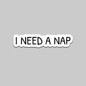 May include: White sticker with the phrase "I NEED A NAP" in black, handwritten-style font. The sticker has a white border and is set against a gray background. The text is centered.