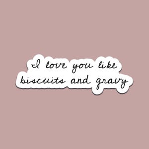 May include: A white sticker with the handwritten text "I love you like biscuits and gravy" in black cursive script. The sticker has a white border and is set against a muted pink background.