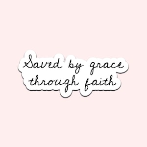 May include: A white sticker with the phrase "Saved by grace through faith" in black cursive script. The sticker has a white border and is set against a light pink background.