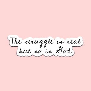 May include: A white sticker with the text "The struggle is real but so is God" in black cursive font. The sticker has a white border and is set against a light pink background.