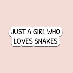 May include: A white sticker with the text "JUST A GIRL WHO LOVES SNAKES" in a black, bold font. The sticker has a rounded, cloud-like border and is set against a light pink background.