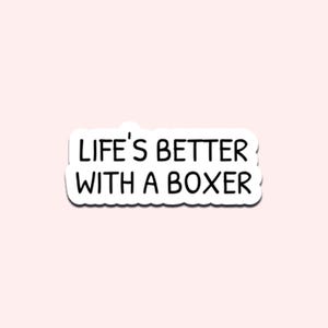 May include: A white sticker with the text "LIFE'S BETTER WITH A BOXER" in black, outlined in white. The sticker is on a light pink background. The sticker is a fun item for dog lovers.